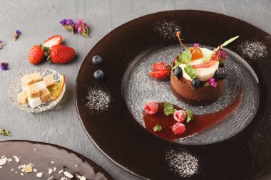 Bir tatlı seti üzerinde krema ve taze meyveler olan çikolatalı bir mus sunar. Çevreleyen öğeler arasında meyve, şeker küpleri ve yenilebilir çiçekler bulunmaktadır..