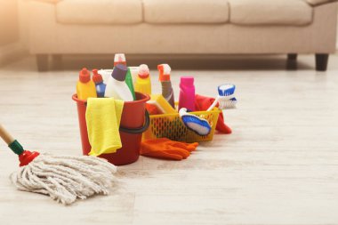 Kanepenin yanındaki ahşap zemine çeşitli temizlik malzemeleri konur. Temizlik işleri için düzenlenmiş kovalar, spreyler ve fırçalar var. Sahne ev işleri için hazırlık gösteriyor..