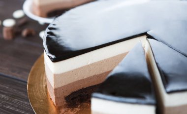 Tahta bir masada farklı pasta katmanları gösterilir. Pastanın altında beyaz ve kahverengi katmanları olan koyu bir üst tabakası vardır. Birkaç dilim kesilmiş ve tatlı malzemeleri de yakınlarda..