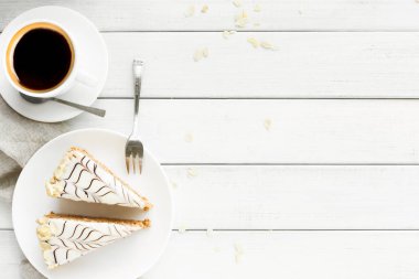 Sıcak bir fincan kahve beyaz bir tabakta iki dilim pastanın yanında oturur. Masa aydınlık ve basit, rahat bir atmosfer yaratıyor. Tabağın yanında bir çatal sizi eğlenmeye davet ediyor..