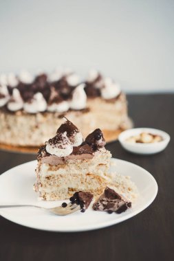 Bir pasta dilimlenmiş bir masada sergilenir ve beyaz bir tabağa yerleştirilir. Dilimin yanında bir çatal duruyor. Bütün pasta arka planda görünüyor..