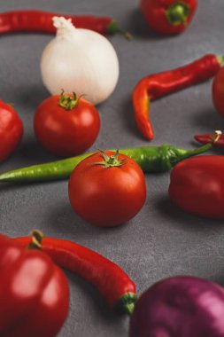 Karanlık bir yüzeyde çeşitli sebzeler sergilenir. Kırmızı domates, yeşil ve kırmızı biber, bir soğan ve diğer öğeler yemek hazırlamak için gelişigüzel bir şekilde düzenlenir..