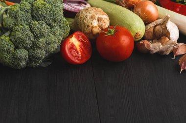 Koyu ahşap bir yüzey üzerinde çeşitli taze sebzeler sergilenir. Seçimde brokoli, domates, kabak ve sarımsak yer alıyor. Bu sebzeler genellikle yemek ve yemek tarifleri için kullanılır..