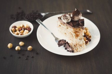 Tatlı sergisi beyaz bir tabakta çikolata ve kremayla kaplı bir dilim pasta içerir. Yakınlarda fındık ve kahve çekirdekleri ile dolu küçük bir kase var..