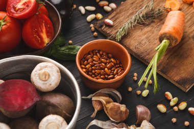 Farklı türde sebzeler ve fasulyeler mutfakta karanlık bir yüzeye dizilir. Eşyalar arasında domates, mantar, sarımsak, havuç ve kahverengi tabaklar ve bir kesim tahtasının etrafına konan fasulyeler yer alıyor..