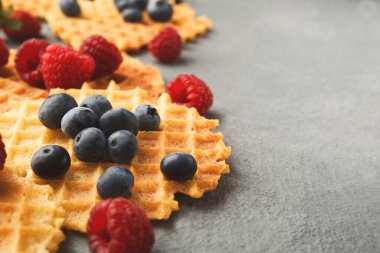 Gri bir yüzeye bir waffle kolajı yerleştirilir. Taze yaban mersini ve ahududu waffle 'ların her tarafına saçılmış. Düzenleme doku ve renklerin bir karışımını gösterir.