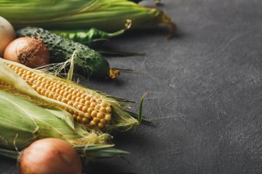 Taze sebzeler karanlık bir yüzeye yerleştirilir. Mısır, soğan, salatalık ve yeşil biber birlikte yemek pişirmek için gösterilir. Bu kurulum yemek hazırlığı için hazır..