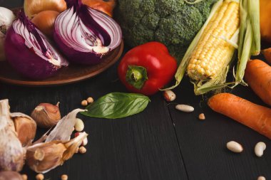 Karanlık bir yüzeyde çeşitli taze sebzeler bir koleksiyonda sergilenir. Sette soğan, brokoli, mısır, dolmalık biber, havuç ve sarımsak yer alıyor. Her parça yemek hazırlığı için hazır..