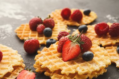 Waffle 'lar üzerinde çilek, ahududu ve yaban mersini olan koyu bir yüzeye yerleştirilir. Sahne, gelişigüzel dizilmiş waffle koleksiyonunu gösteriyor..