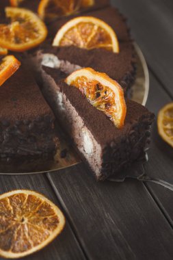 Yuvarlak bir tabakta üzerinde kurumuş portakal dilimleri olan bir çikolatalı pasta sergilenir. Bir dilim pasta kesilip çıkarıldı ve içinin zenginliği ortaya çıktı..