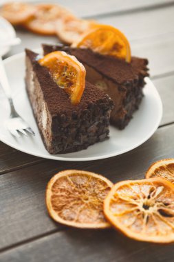 Kurutulmuş portakal dilimli iki dilim çikolatalı pasta beyaz bir tabakta servis edilir. Tabak ahşap bir masanın üzerine konur. Bu sahne eğlenmek için yaratılmış ve davet ediliyor..