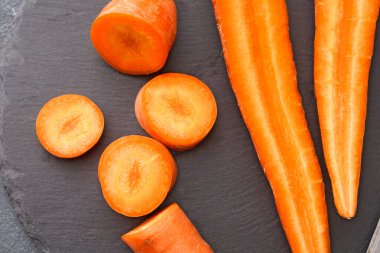 Havuçlar siyah taş bir yüzeye yerleştirilir. Yuvarlak dilimler ve çubuklar da dahil olmak üzere çeşitli şekillerde kesilmiş. Canlı turuncu renk koyu arkaplanda göze çarpıyor..