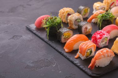 Farklı suşi türleri siyah bir tabakta sergilenir. Koleksiyonda börek, sashimi ve diğer suşi parçaları yer alıyor. Suşi renkli malzemeler ve yaratıcı tasarımlar içerir..