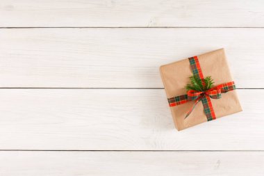 Kahverengi kağıda sarılı bir hediye beyaz ahşap bir yüzeye yerleştirilir. Pakette ekose bir kurdele ve bir dal yeşillik var. Bu ayar basit, şenlikli bir düzenleme gösteriyor.