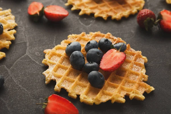 Bir koleksiyonda koyu bir yüzeye yerleştirilmiş taze çilek ve yaban mersinli waffle 'lar yer alır. Set, waffle 'ların farklı açılarını ve bölümlerini gösterir..