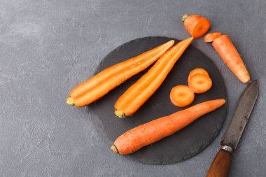 Taze havuçlar siyah bir kesme tahtasına dizilir. Bazı havuçlar bir bütün, diğerleri ise yuvarlak parçalara bölünmüş. Mutfak bıçağı havuçların yanına konur..