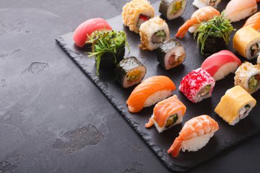 Bir suşi rulosu seti düzgün bir şekilde koyu bir tahta üzerine dizilir. Nigiri ve maki de dahil olmak üzere farklı suşi çeşitleri çeşitli renkler ve malzemeler sergiler..