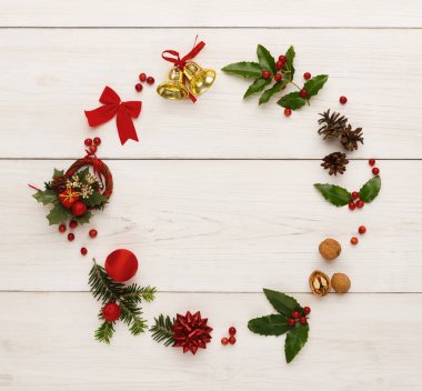 Kırmızı fiyonklar, çanlar ve yeşil yapraklar gibi dekoratif eşyalar daire şeklinde dizilir. Bu şenlik düzeneği bir bayramı kutlamak için mükemmel. Arka plan basit bir tahta yüzey..