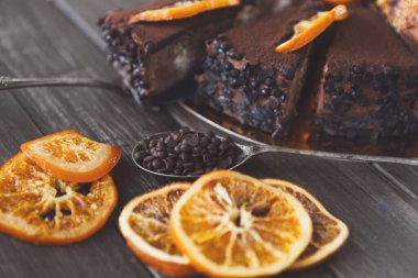 Üzerinde portakal dilimleri ve yanında kurutulmuş portakal parçaları olan çikolatalı bir pasta seti. Sahne ahşap bir masanın üzerinde tatlı ikram ediliyor..