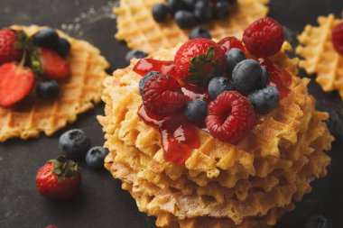 Bir yığın waffle siyah bir tabağa konur. Waffle 'lar taze ahududu, yabanmersini ve bir kat çilek reçeli ile kaplıdır. Bu ekran kahvaltı zevkini davet eder.