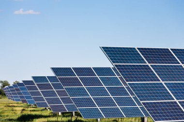 Güneş panelleri açık bir alanda, açık mavi gökyüzünün altında kurulur. Güneş panelleri enerji üretimi için güneş ışığını yakalamak üzere konumlandırılmıştır..