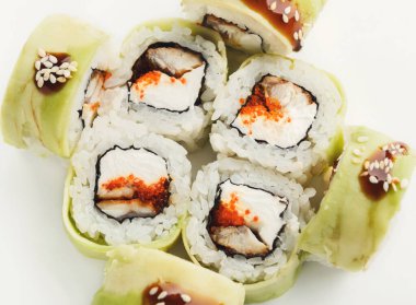 Sade beyaz bir yüzey üzerinde bir suşi rulosu sergilenir. Her rulo pirinç, balık ve malzemeler içeriyor. Düzenleme, ruloların çeşitliliğini ve detaylarını gösteriyor ve görüntülerini büyütüyor..