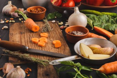 Taze sebzeler ahşap bir masada düzenlenir. Havuç, domates ve bitkiler görülebilir. Yakınlarda bir bıçak duruyor..