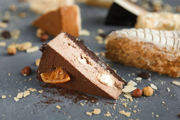 Çeşitli pasta ve tatlılardan oluşan bir kolaj gri bir yüzeyde sunulmaktadır. Karışımda çikolatalı mus, katmanlı kek ve çıtır çıtır soslar yer alıyor..