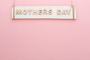Anneler Günü 'nün pembe duvarda asılı olduğu tahta bir tabela. Tabela sade ve arka plan katı bir renk. Bu düzen, anneleri onurlandırma temasına odaklanıyor..