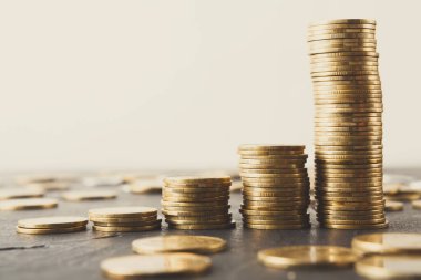 Yığılan paralar düz bir yüzeyde farklı yükseklikler oluşturur ve etrafa saçılmış paralar. İçerisi tarafsız bir arka planla çevrili. Odak noktamız paralar ve onların düzenlemeleri..