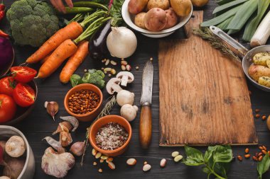 Taze sebze koleksiyonu ahşap bir masada düzenlenir. Domates, havuç, patates ve otlar görülebilir. Pişirme aletleri sebzelerin yanına yerleştirilir, hazırlanmaya hazır..