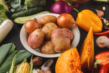 Çeşitli sebzeler siyah bir masaya konur, renkli bir kolaj oluştururlar. Ortada bir kase patates var. Çevrelerinde salatalık, biber, soğan ve daha bir çok şey vardır..