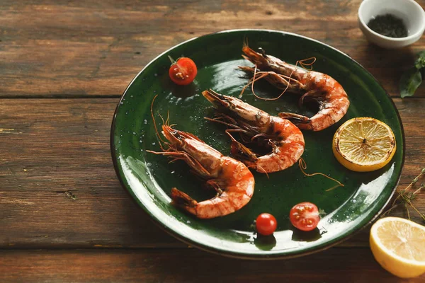 Yeşil bir tabakta limon dilimleri ve vişneli domateslerin yanında üç karides düzenlenir. Ahşap bir masa içermesi çok basit. Taze malzemeler renk ve doku ekler.