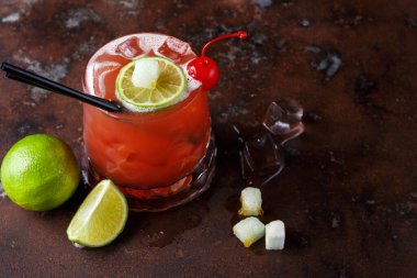 Bir kokteyl, buz ve süslemelerle dolu karanlık bir yüzeye oturur. İçkinin yanında parlak bir renk, limon dilimleri, kiraz ve şeker küpleri var. Camın yanında bir kireç ikiye bölünmüş..