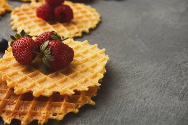 Waffle 'lar gri bir yüzeye istiflenmiş taze çilek ve yaban mersini ile kaplıdır. Bu yemek gösterisi her zaman tatlı kahvaltı seçeneklerini ön plana çıkarır..