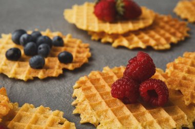 Waffle parçaları düz bir yüzeye rastgele dizilir. Çilek, yabanmersini ve ahududu gibi çeşitli meyveler waffle parçalarının üzerine konur..