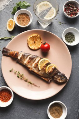 Izgara balık hafif bir tabağa konur. Limon dilimleri, bir domates ve baharatlı çeşitli kaseler. Yakında bir bardak su var. Yemek hazırlama sahnesini gösteriyor..