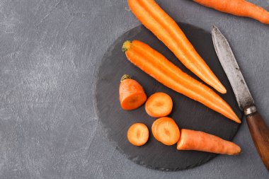 Koyu gri bir yüzeye bir sürü havuç ve kesilmiş havuç yerleştirilir. Havuçların yanına bir bıçak yerleştirilir. Bu düzen muhtemelen yemek hazırlama ya da pişirme içindir..