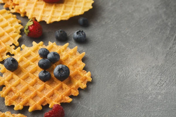 Waffle 'lar gri bir yüzeye yerleştirilir. Waffle 'ların etrafına taze çilek ve yabanmersini saçılmış. Bu sahne, basit yemek öğünleri içeren bir sabah yemeği hazırlıyor..