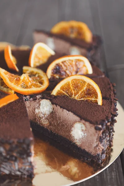 İçinde portakal dilimleriyle süslenmiş çikolatalı pasta olan bir tatlı seti. Pasta dilimlenmiş. İçi kremalı. Sahne ahşap bir masanın üzerine kurulmuş..
