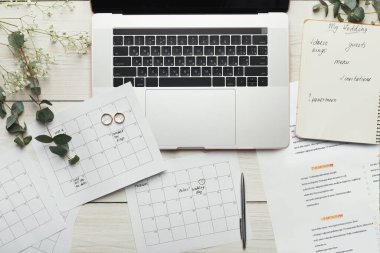 Takvimler ve düğün notları, tahta bir masadaki dizüstü bilgisayarın etrafında düzenlenir. İki yüzük kağıtların yanında duruyor. Bu sahnenin odak noktası düğün hazırlıkları..