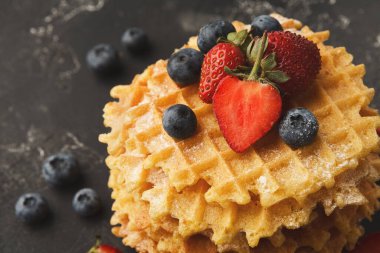 Karanlık bir yüzeye bir yığın waffle konur. Taze çilekler ve yaban mersinleri waffle 'ların üzerinde düzenlenir. Sahne günün her saatinde lezzetli bir tatlıyı gösteriyor..