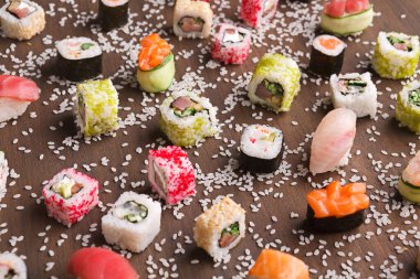 Ahşap bir yüzeyde çeşitli suşi ruloları düzenlenir. Farklı şekiller ve renkler suşiyi oluşturur. Sushi 'nin etrafına küçük susam tohumları serpiştirilir. Bu paylaşım için bir yemek seti..