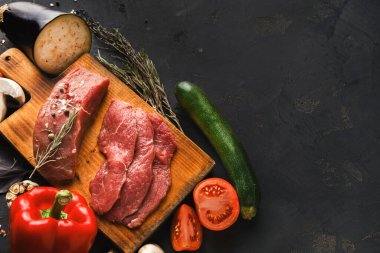 Renkli taze sebze koleksiyonu ve et kesimleri ahşap bir tahta üzerinde düzenlenir. İçindekiler arasında kabak, domates, kırmızı biber ve bitkiler yer alıyor. Sahne yemek pişirmek için iyi hazırlanmış..