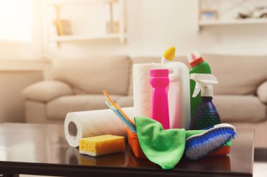 Temizlik malzemeleri odadaki bir masanın üzerine konur. Şişeler, süngerler, bezler ve kağıt havlular. Güneş ışığı pencereden içeri giriyor..
