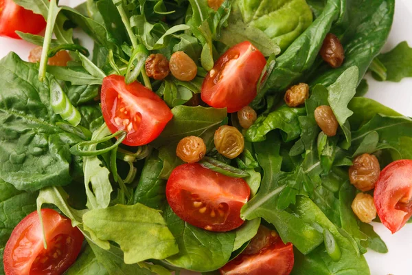 Çeşitli sebze çeşitleri, yarım kiraz domatesleri ve küçük kuru üzümlerden oluşan taze bir salata beyaz bir tabakta güzelce düzenlenir. Bu yemek renk ve dokuların karışımını sunar..