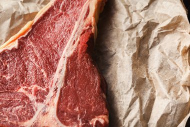 Buruşuk kahverengi kağıt üzerinde yapılan çiğ et kesikleri koleksiyonu çeşitli sığır eti türlerini sergiliyor. Sahne, mutfak ortamındaki farklı etlerin dokularını ve renklerini vurguluyor..