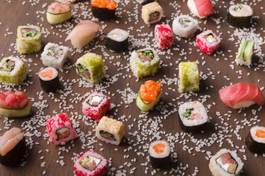 Çeşitli suşi türlerinin bir koleksiyonu ahşap bir masanın üzerine serilmiştir. Farklı renkler ve şekiller canlı bir görüntü oluşturur.