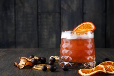 Kurutulmuş meyve dilimleri ve böğürtlenlerin yanına bir içki konur. İçkinin kenarında bir dilim portakal ve bardağın içinde kabarcıklar var..