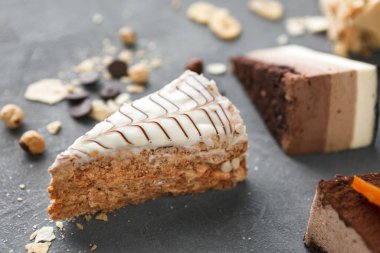 Bir dilim pasta, farklı tatlılarla çevrili karanlık bir yüzeyde oturur. Çikolata ve tahıl parçaları etrafa saçıldı. Bu renkli bir yemek kolajı yaratır..